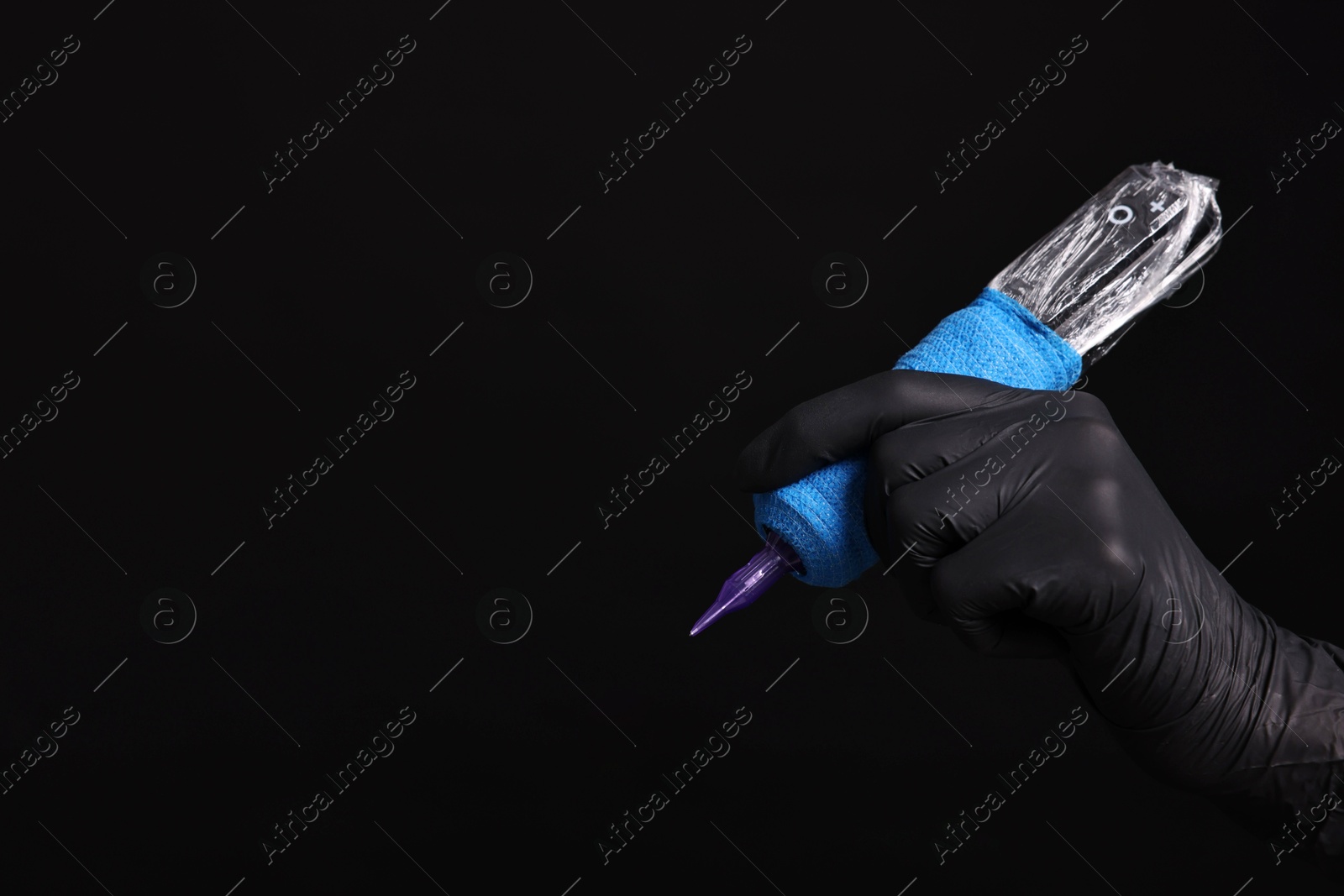 Photo of Professional artist in gloves holding tattoo machine on black background, closeup. Space for text