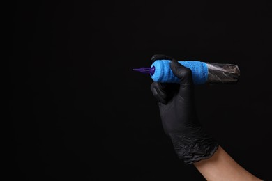 Photo of Professional artist in gloves holding tattoo machine on black background, closeup. Space for text