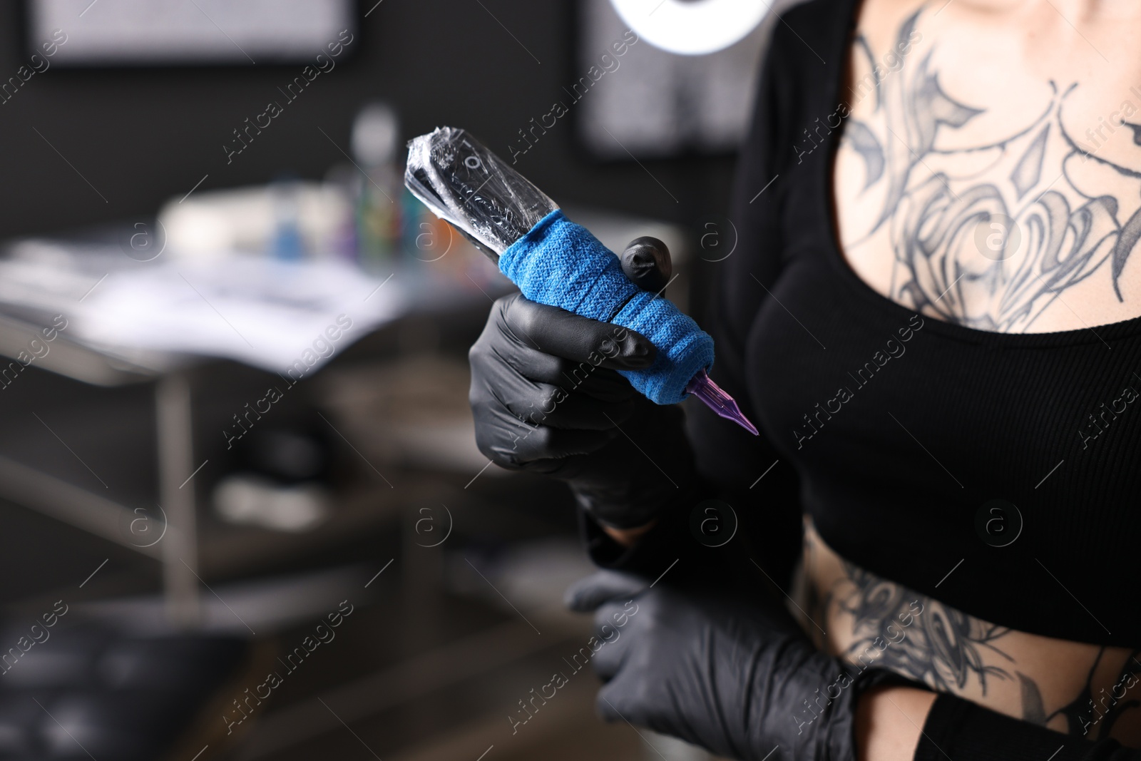 Photo of Professional artist in gloves with tattoo machine in salon, closeup. Space for text