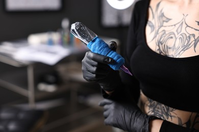 Photo of Professional artist in gloves with tattoo machine in salon, closeup. Space for text