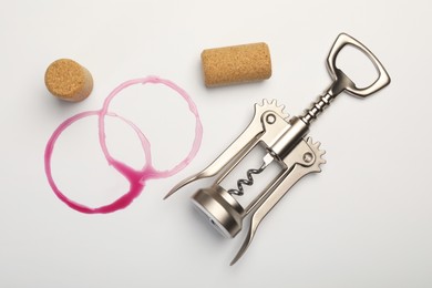 Photo of Wing corkscrew, corks and red wine stains on white background, top view