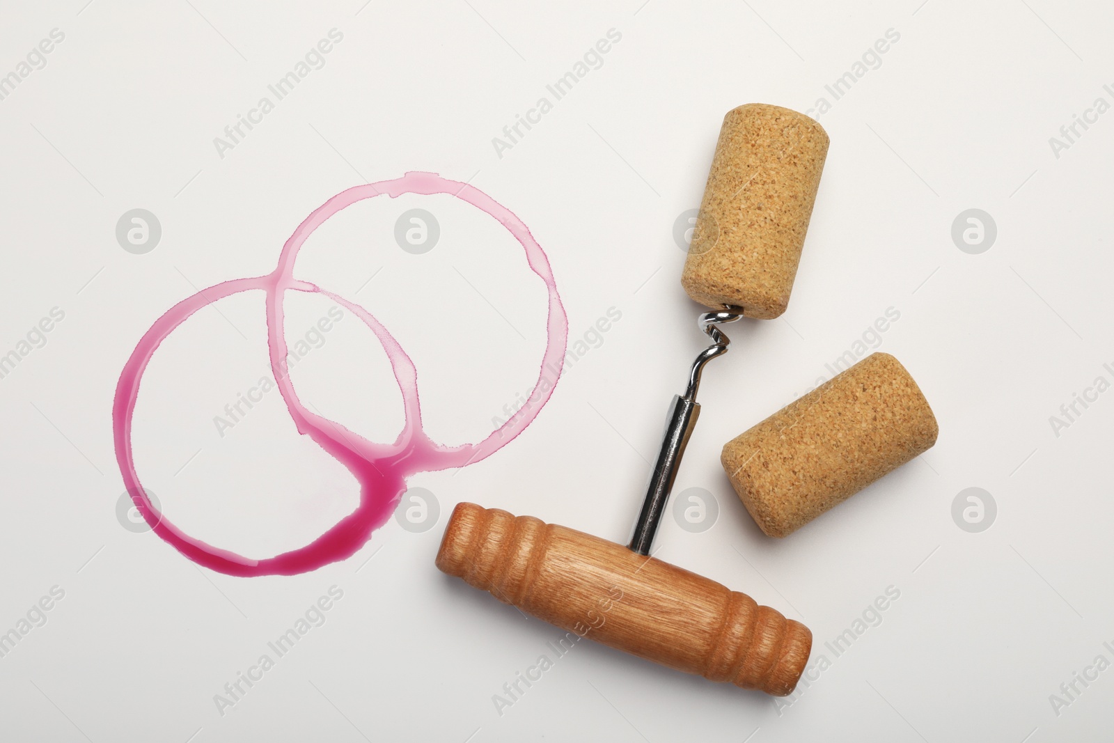 Photo of Corkscrew, cork and red wine stains on white background, top view