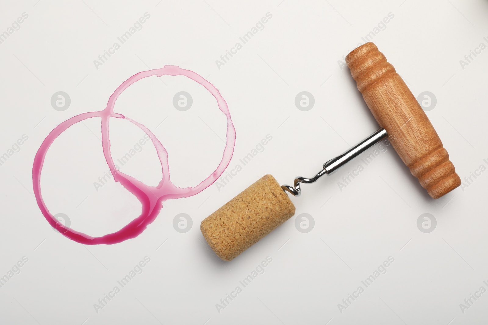 Photo of Corkscrew, cork and red wine stains on white background, top view