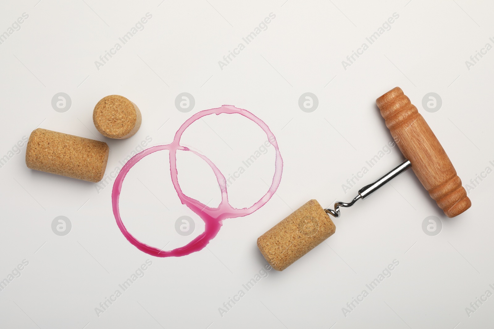 Photo of Corkscrew, corks and red wine stains on white background, top view