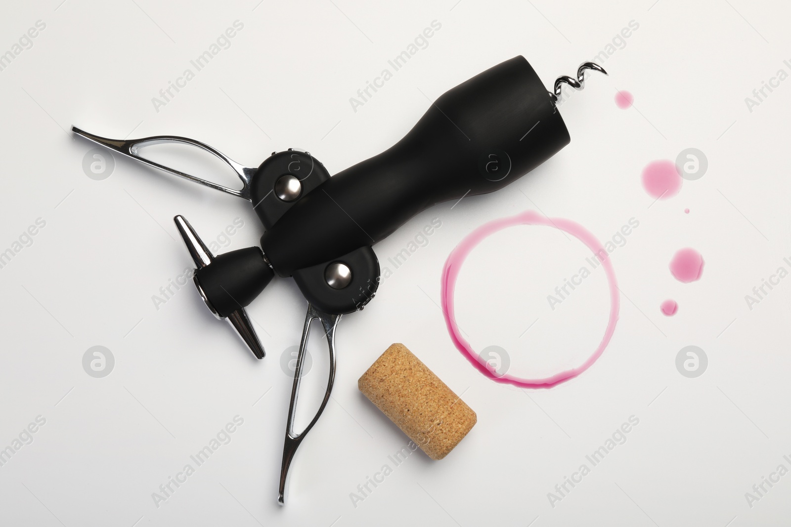 Photo of Wing corkscrew, cork and red wine stains on white background, top view