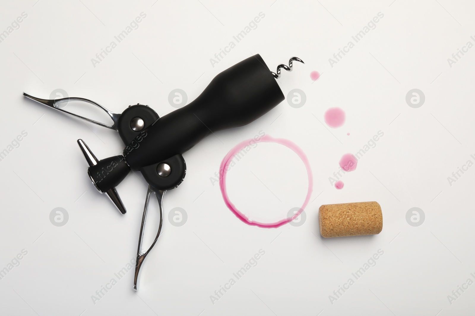 Photo of Wing corkscrew, cork and red wine stains on white background, top view