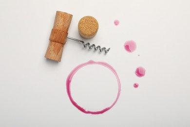 Photo of Corkscrew, cork and red wine stains on white background, top view