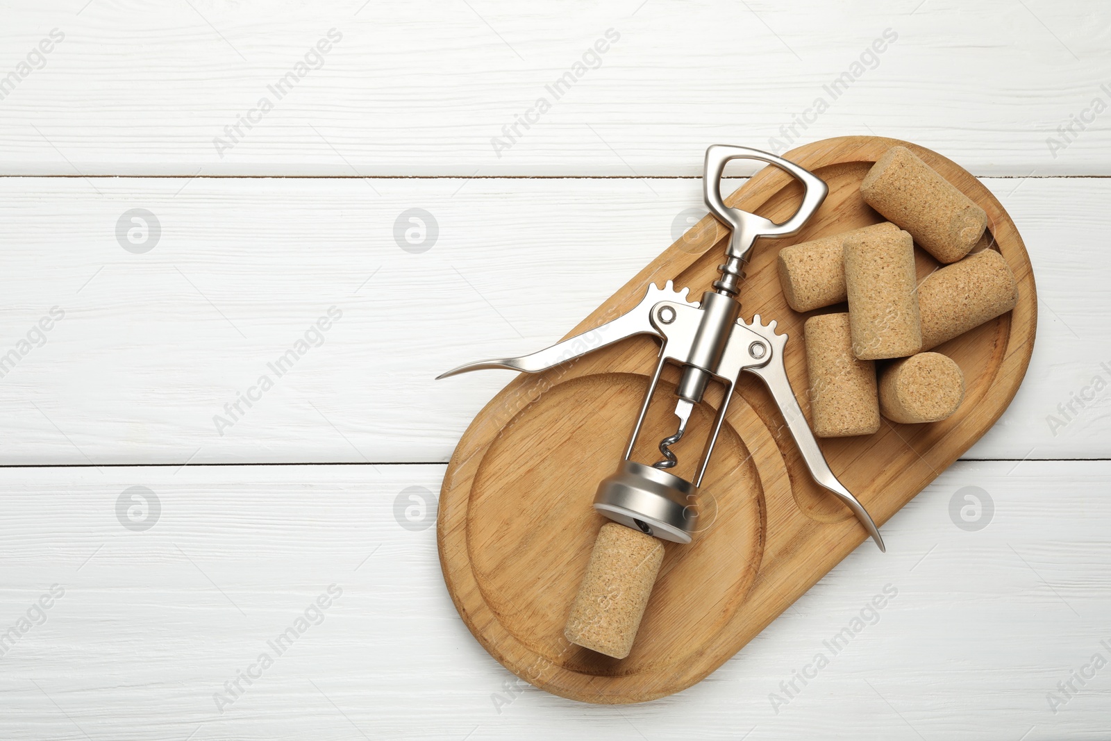 Photo of Wing corkscrew and corks on white wooden table, top view. Space for text