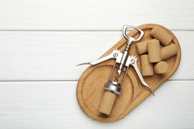 Photo of Wing corkscrew and corks on white wooden table, top view. Space for text