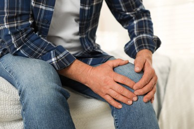 Photo of Senior man suffering from pain in knee at home, closeup