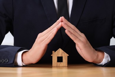 Photo of Property insurance. Real estate agent protecting house figure at table, closeup