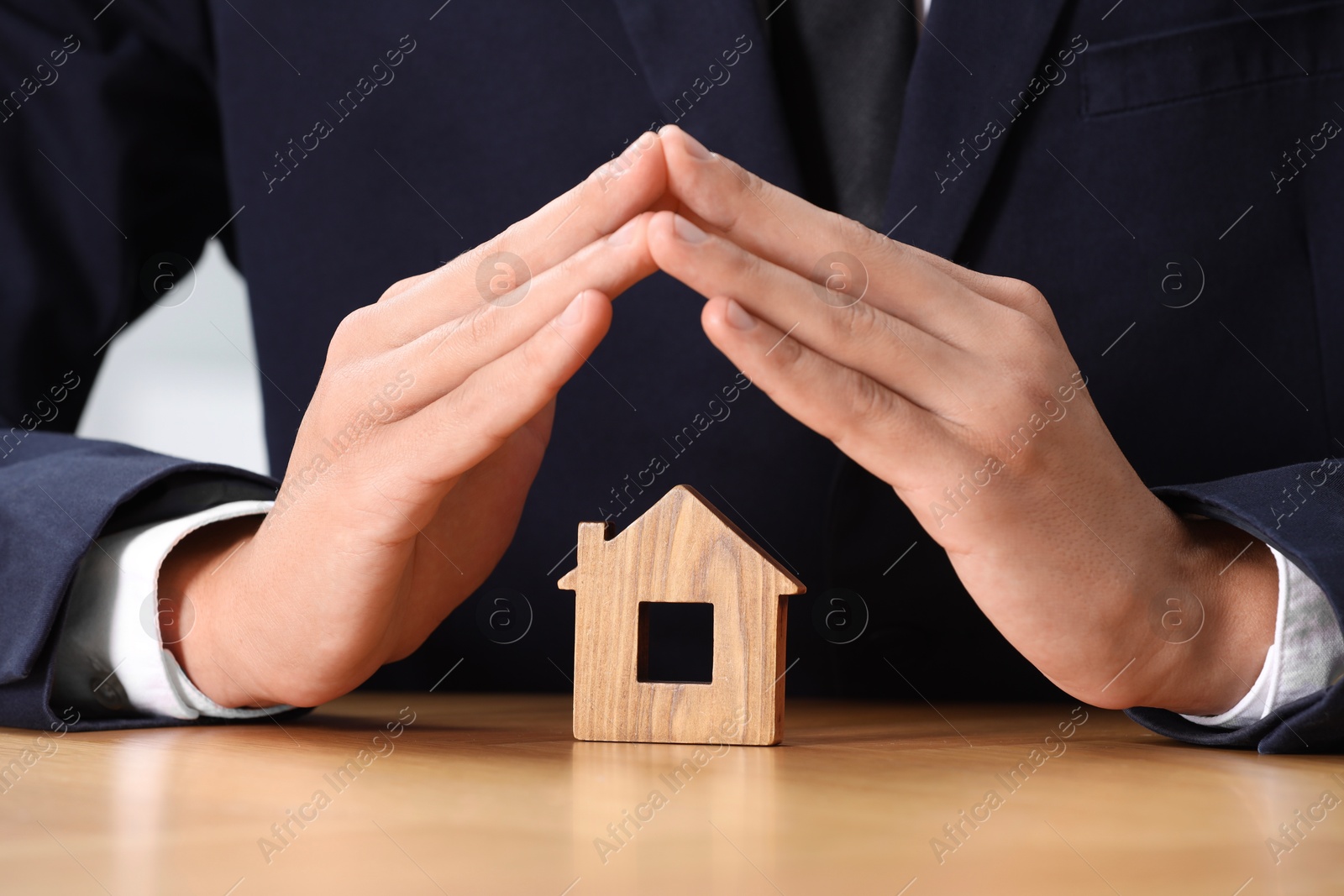 Photo of Property insurance. Real estate agent protecting house figure at table, closeup