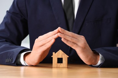 Photo of Property insurance. Real estate agent protecting house figure at table, closeup