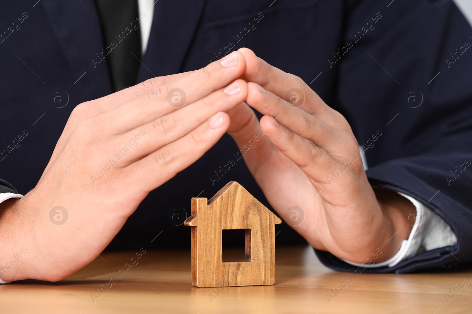 Photo of Property insurance. Real estate agent protecting house figure at table, closeup