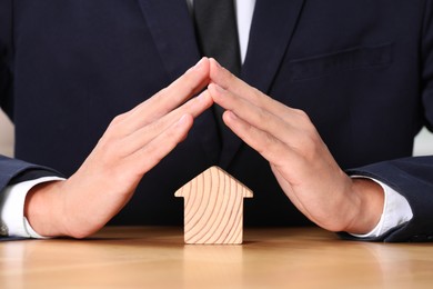 Photo of Property insurance. Real estate agent protecting house figure at table, closeup