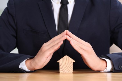 Photo of Property insurance. Real estate agent protecting house figure at table, closeup