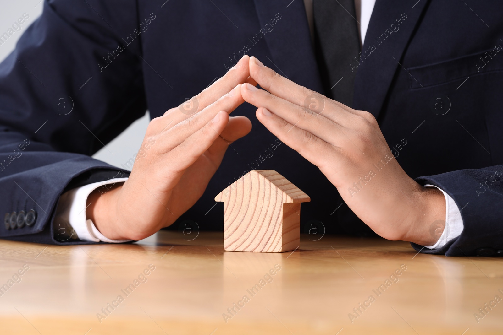 Photo of Property insurance. Real estate agent protecting house figure at table, closeup