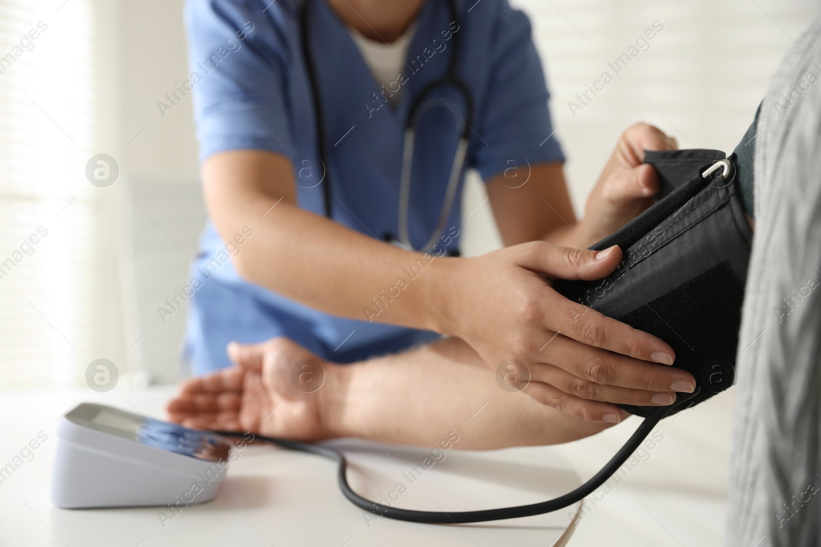 Photo of Doctor measuring patient's blood pressure at table indoors, closeup