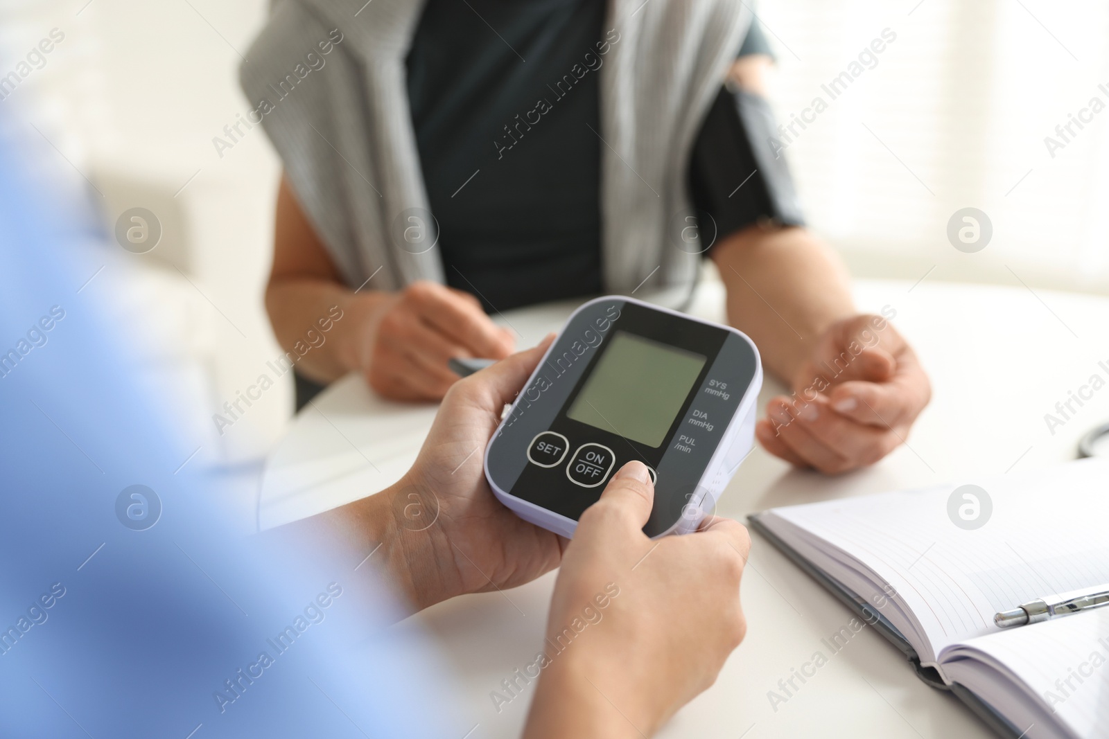 Photo of Doctor measuring patient's blood pressure at table indoors, closeup