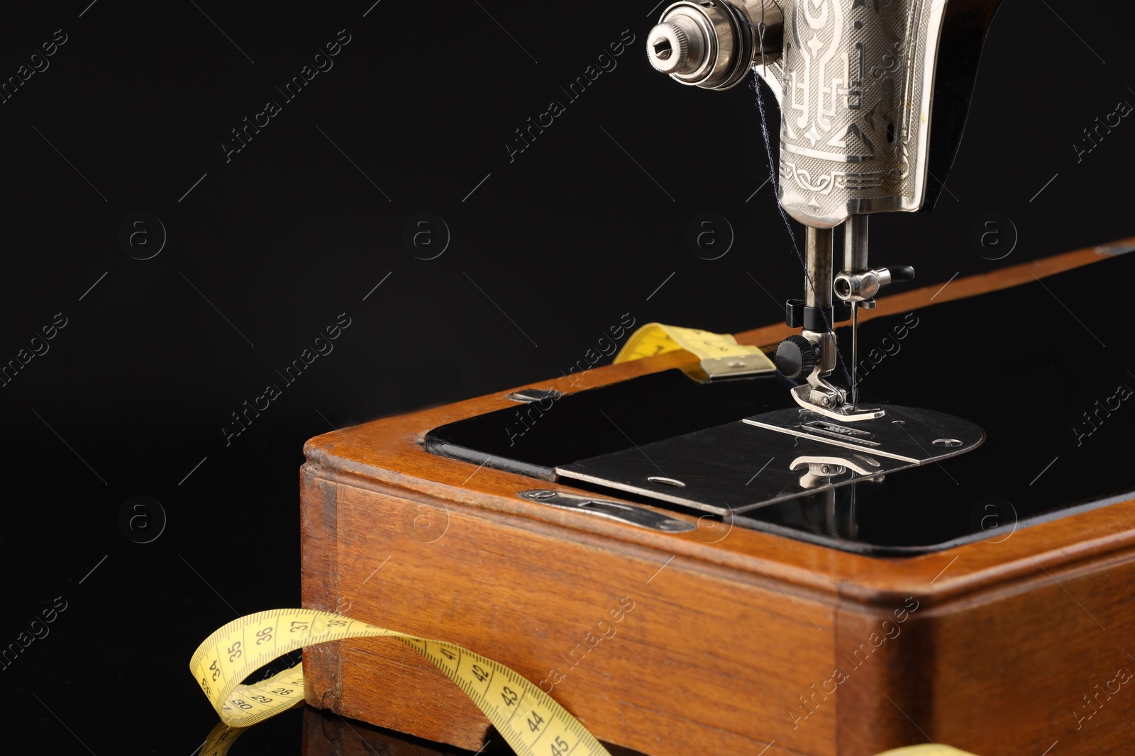 Photo of Professional sewing machine and measuring tape on black background, closeup