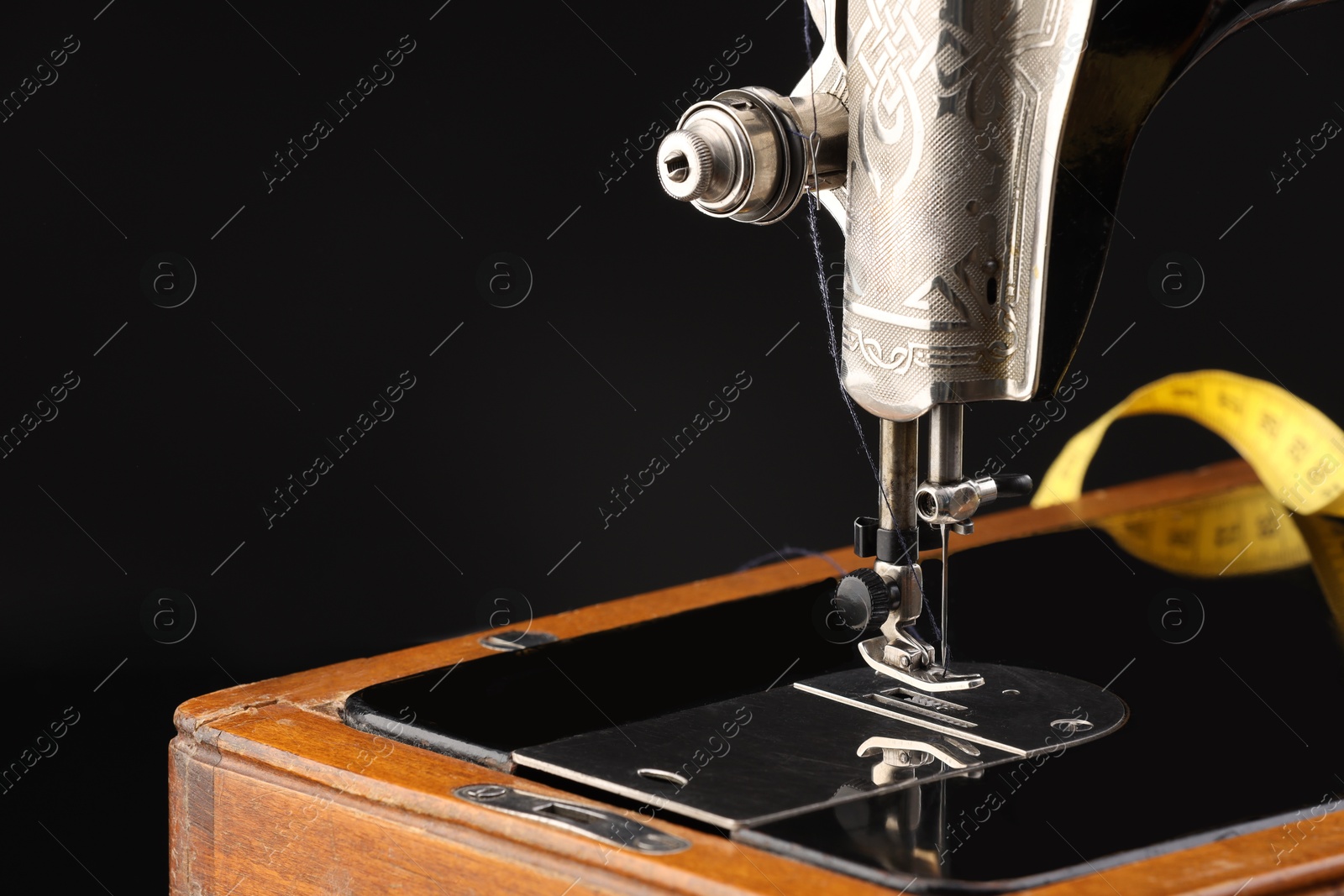 Photo of Professional sewing machine and measuring tape on black background, closeup