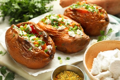 Photo of Tasty cooked sweet potatoes with feta cheese, green onion and parsley on table, closeup