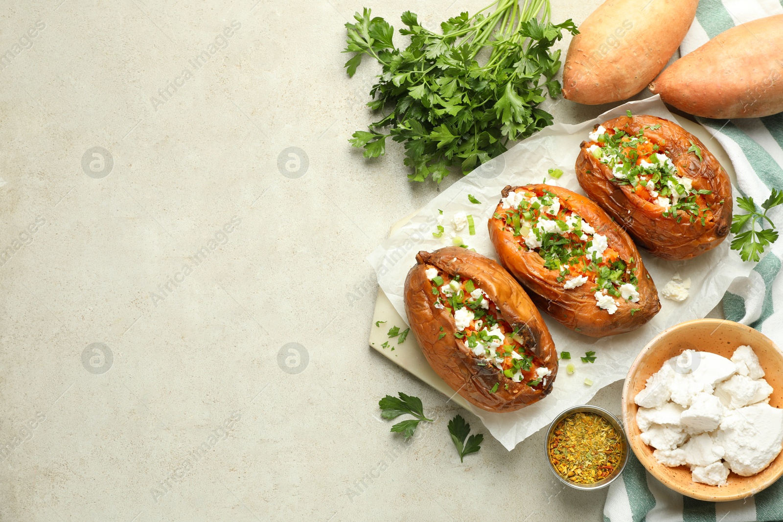 Photo of Tasty cooked sweet potatoes with feta cheese, green onion and parsley on gray textured table, flat lay. Space for text