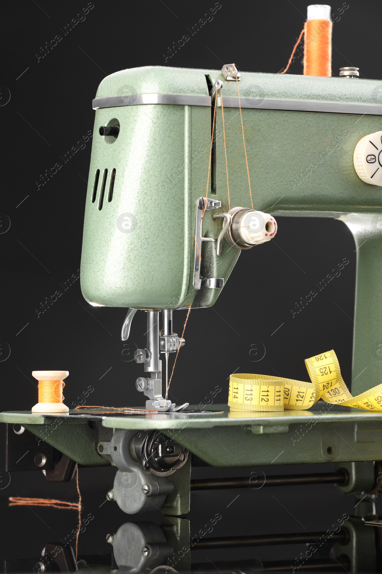 Photo of Professional sewing machine and measuring tape on black background, closeup