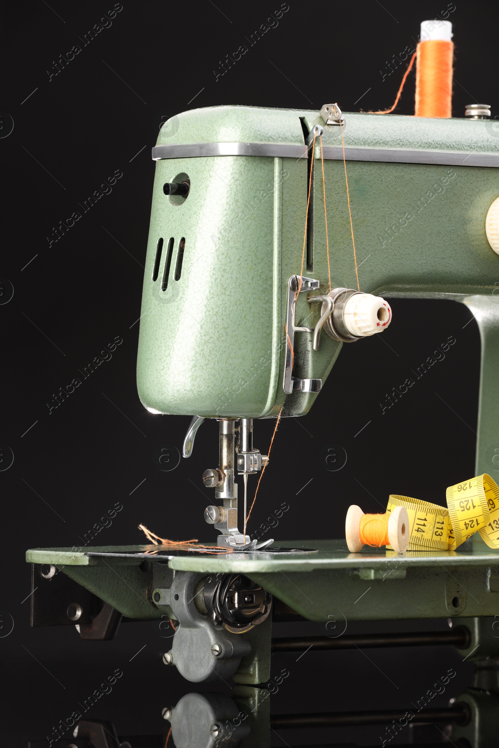 Photo of Professional sewing machine and measuring tape on black background, closeup