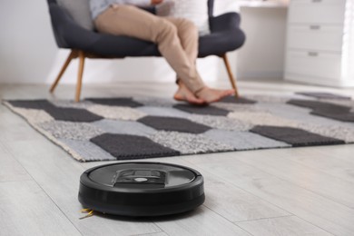 Photo of Young man resting on sofa at home, focus on robotic vacuum cleaner