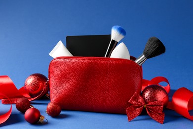 Photo of Christmas gift. Decorative cosmetics in red makeup bag and festive decor on blue background