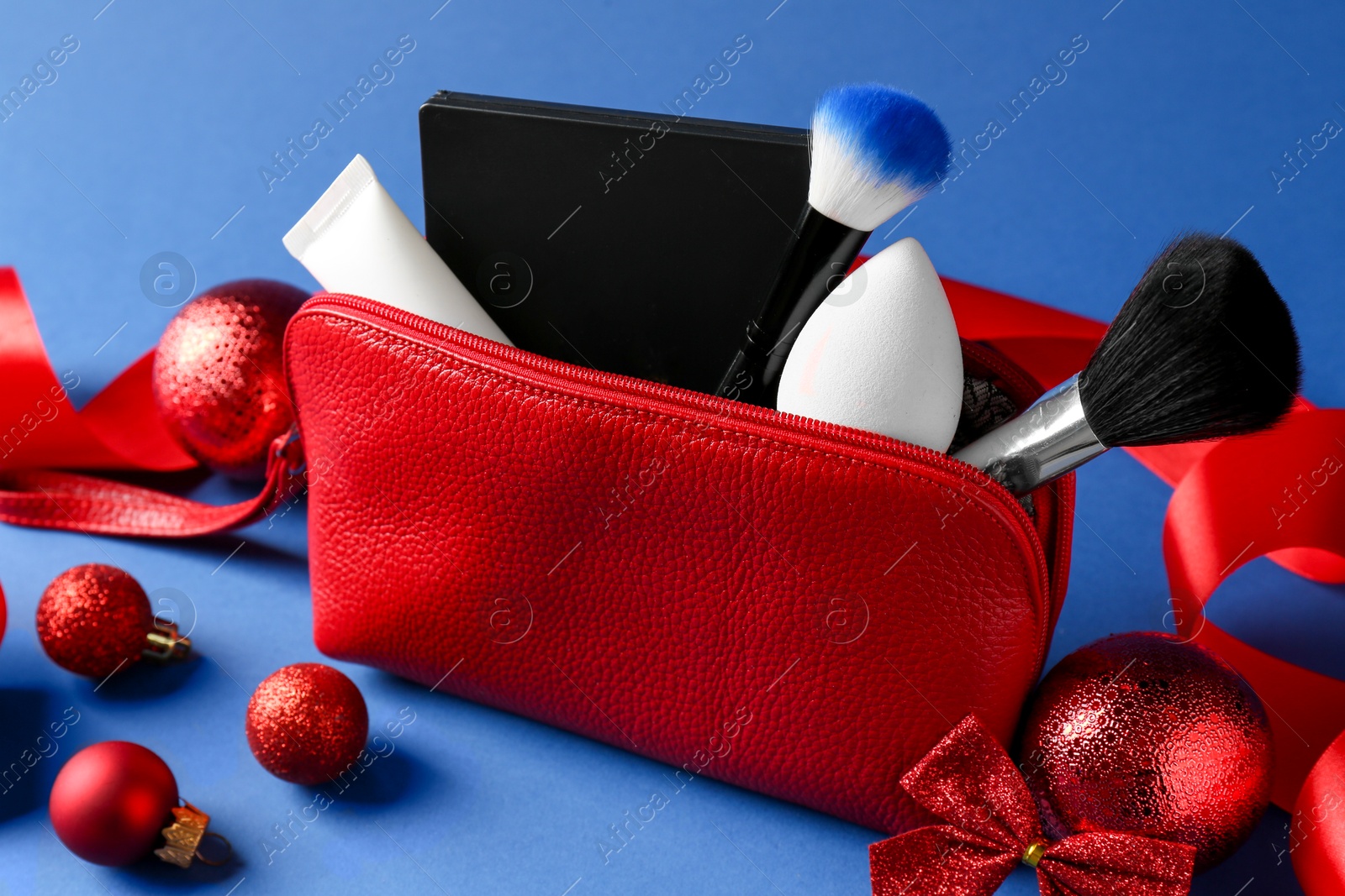 Photo of Christmas gift. Decorative cosmetics in red makeup bag and festive decor on blue background, closeup