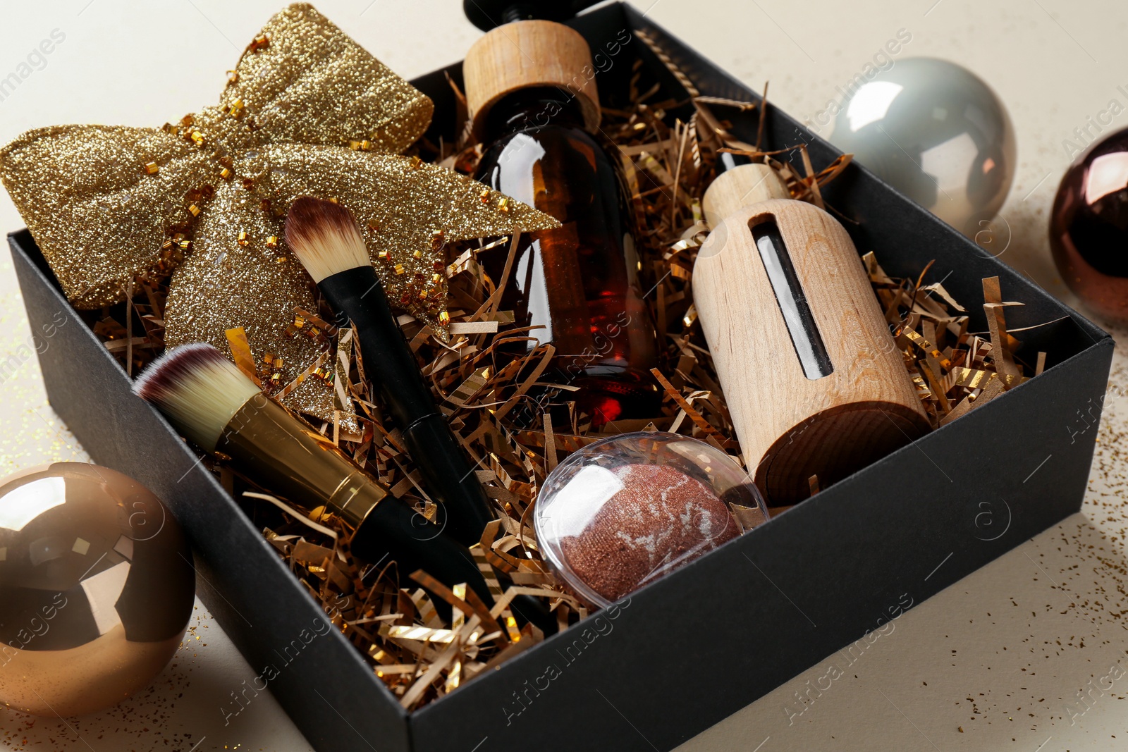 Photo of Christmas gift box with cosmetic products and festive balls on beige background, closeup