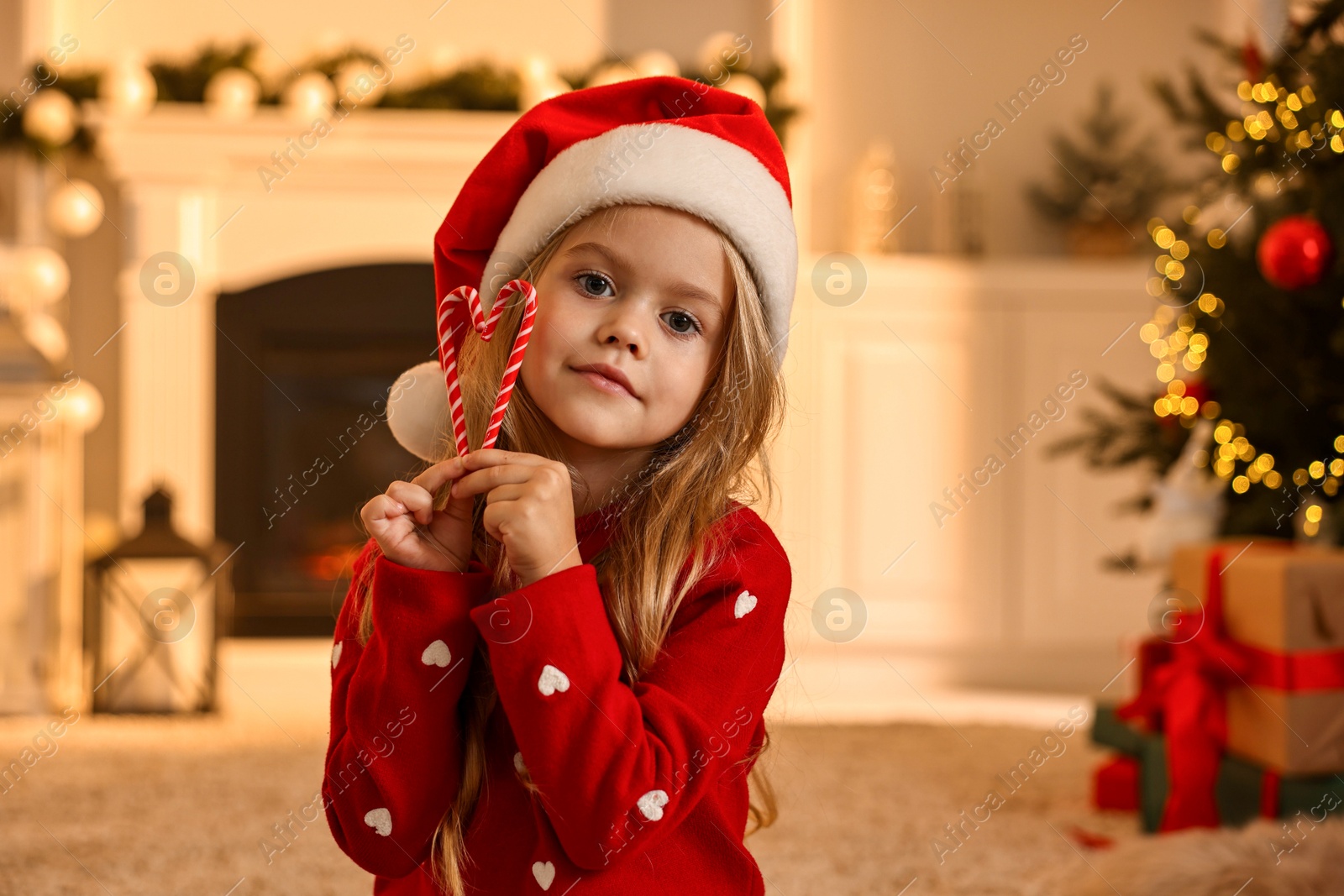 Photo of Little girl in Santa hat with candy canes at home. Christmas celebration