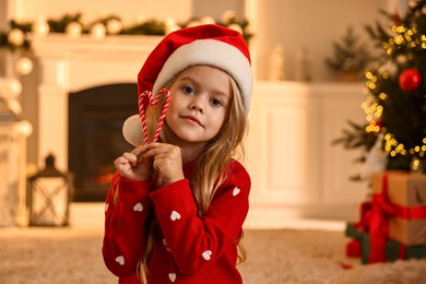 Little girl in Santa hat with candy canes at home. Christmas celebration