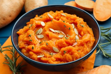Photo of Tasty mashed sweet potato with pumpkin seeds in bowl, fresh vegetables and rosemary on blue wooden table, closeup