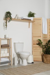 Photo of Folding screen, toilet bowl and houseplant in restroom. Interior design