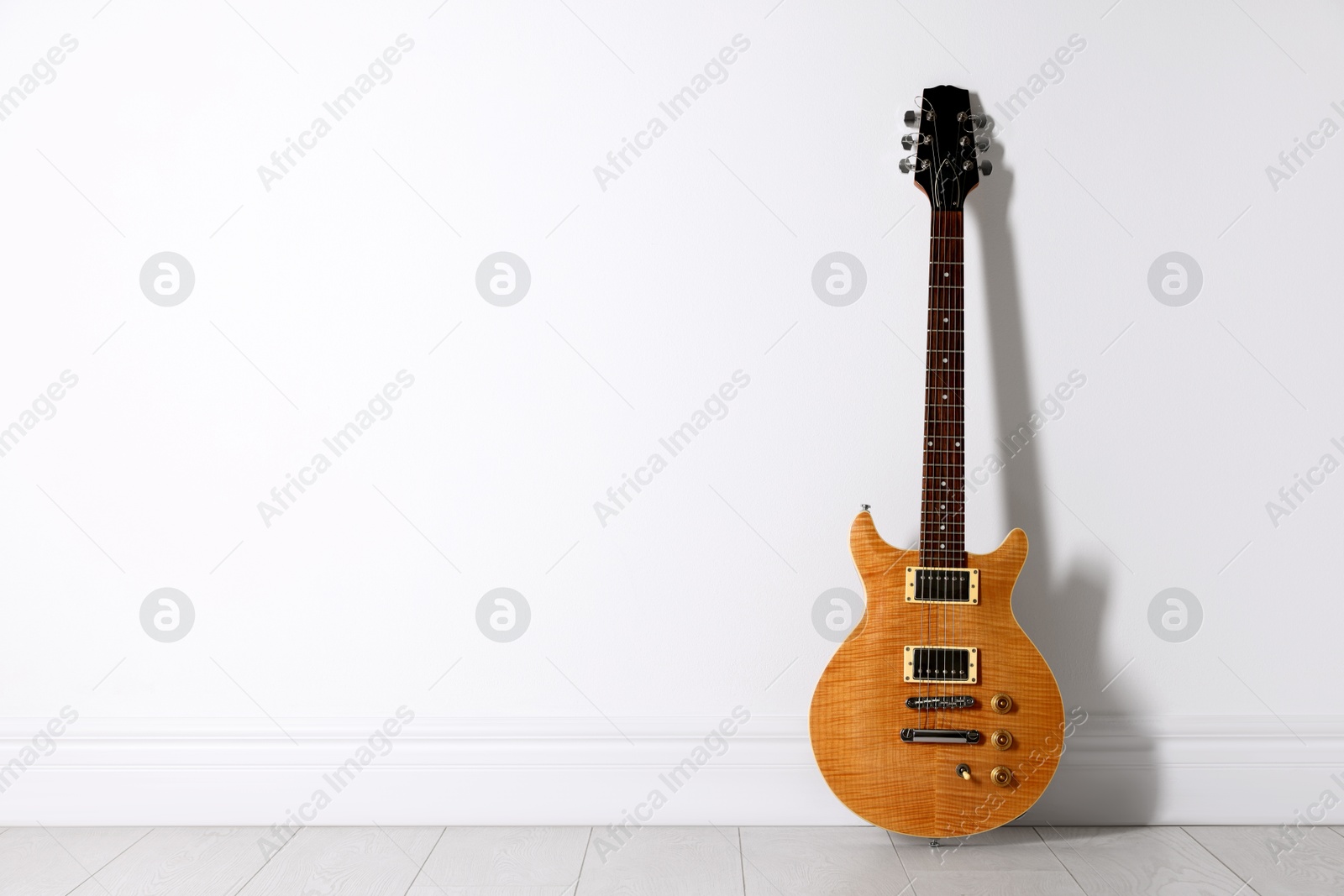 Photo of One modern electric guitar near white wall. Space for text