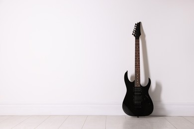 Photo of One modern electric guitar near white wall. Space for text