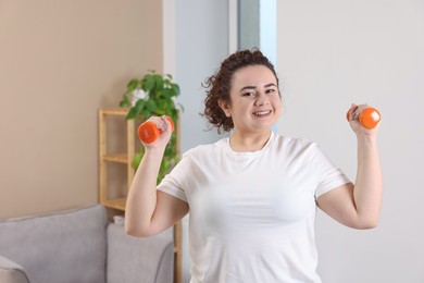 Photo of Plus size woman with dumbbells training at home