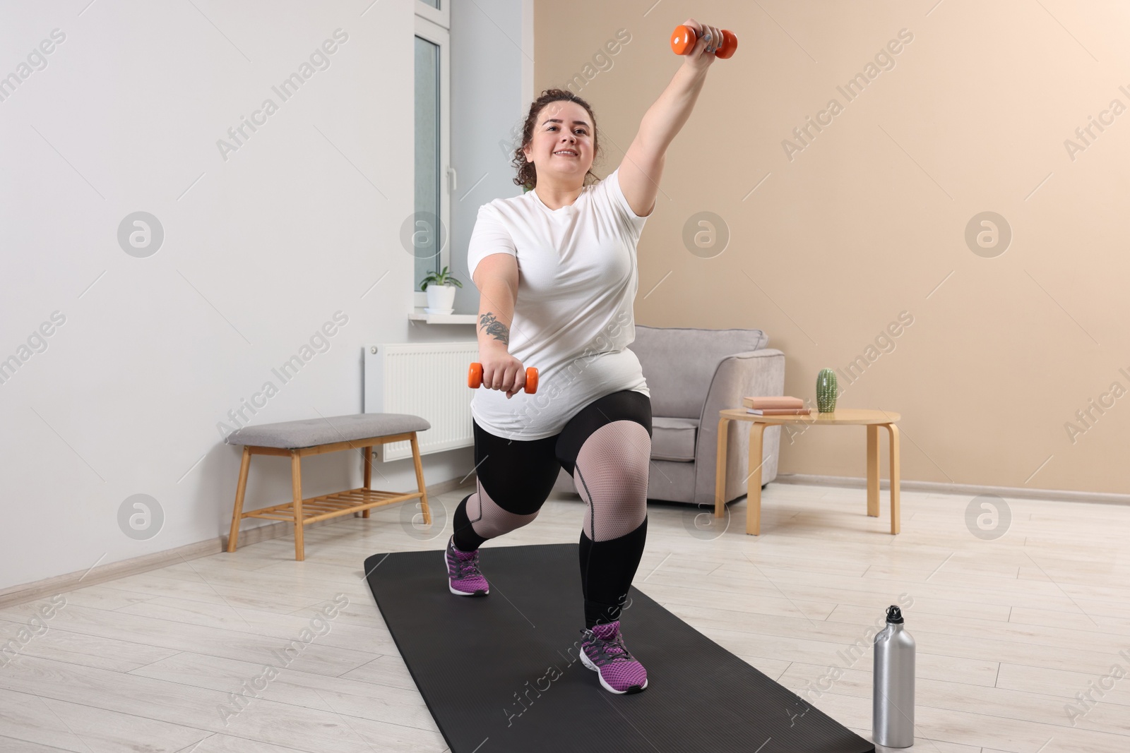 Photo of Plus size woman with dumbbells training at home