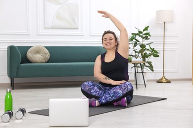 Photo of Plus size woman having fitness training with online coach via laptop at home