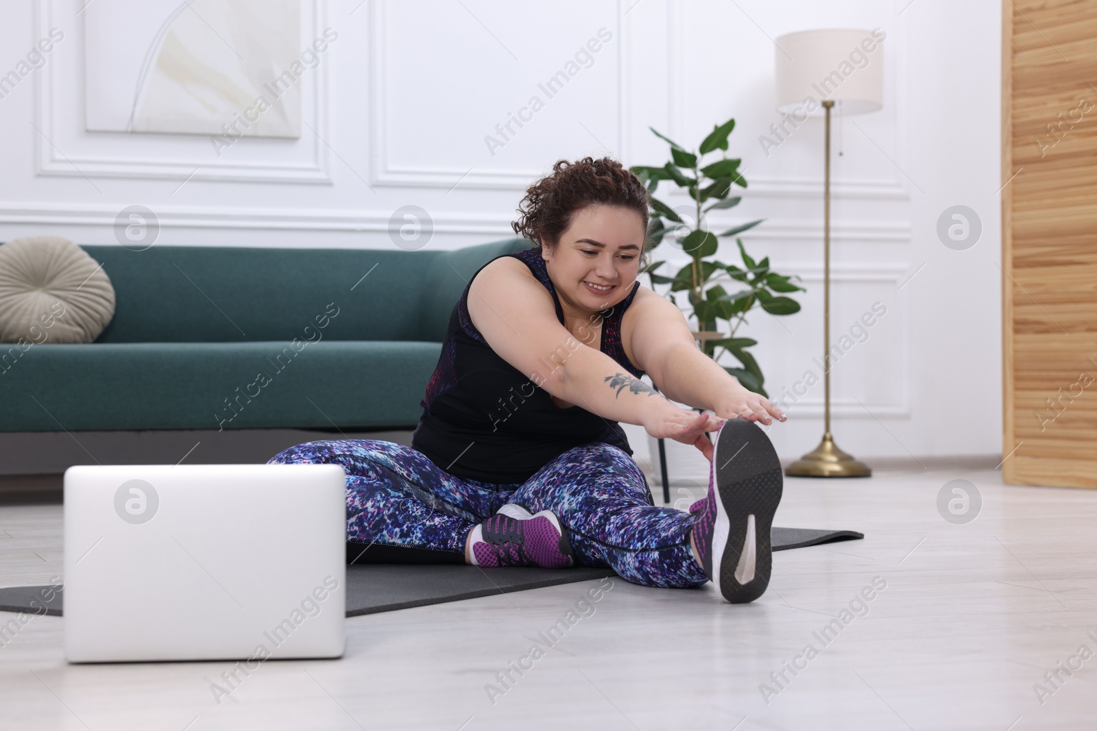 Photo of Plus size woman having fitness training with online coach via laptop at home