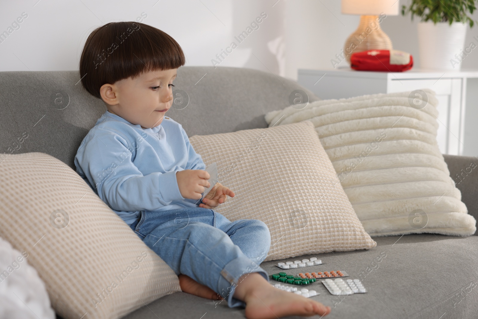 Photo of Little boy playing with pills on sofa at home. Child in danger