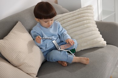 Photo of Little boy playing with pills on sofa at home. Child in danger