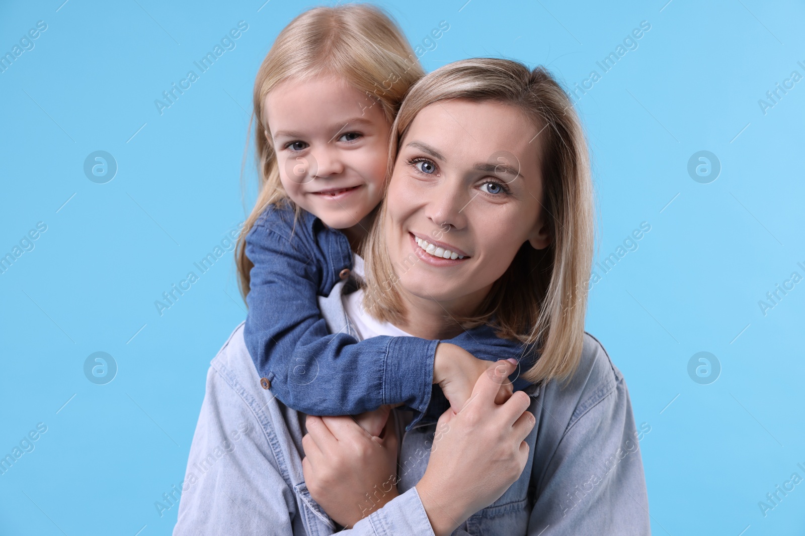 Photo of Cute little girl hugging her mom on light blue background. Happy Mother's Day