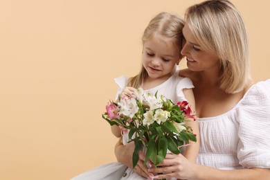 Photo of Little daughter congratulating her mom with bouquet of alstroemeria flowers on beige background, space for text. Happy Mother's Day