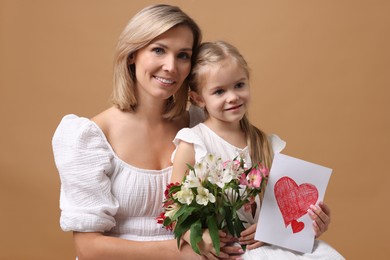 Photo of Happy woman with her daughter, bouquet of alstroemeria flowers and greeting card on beige background. Mother's Day celebration