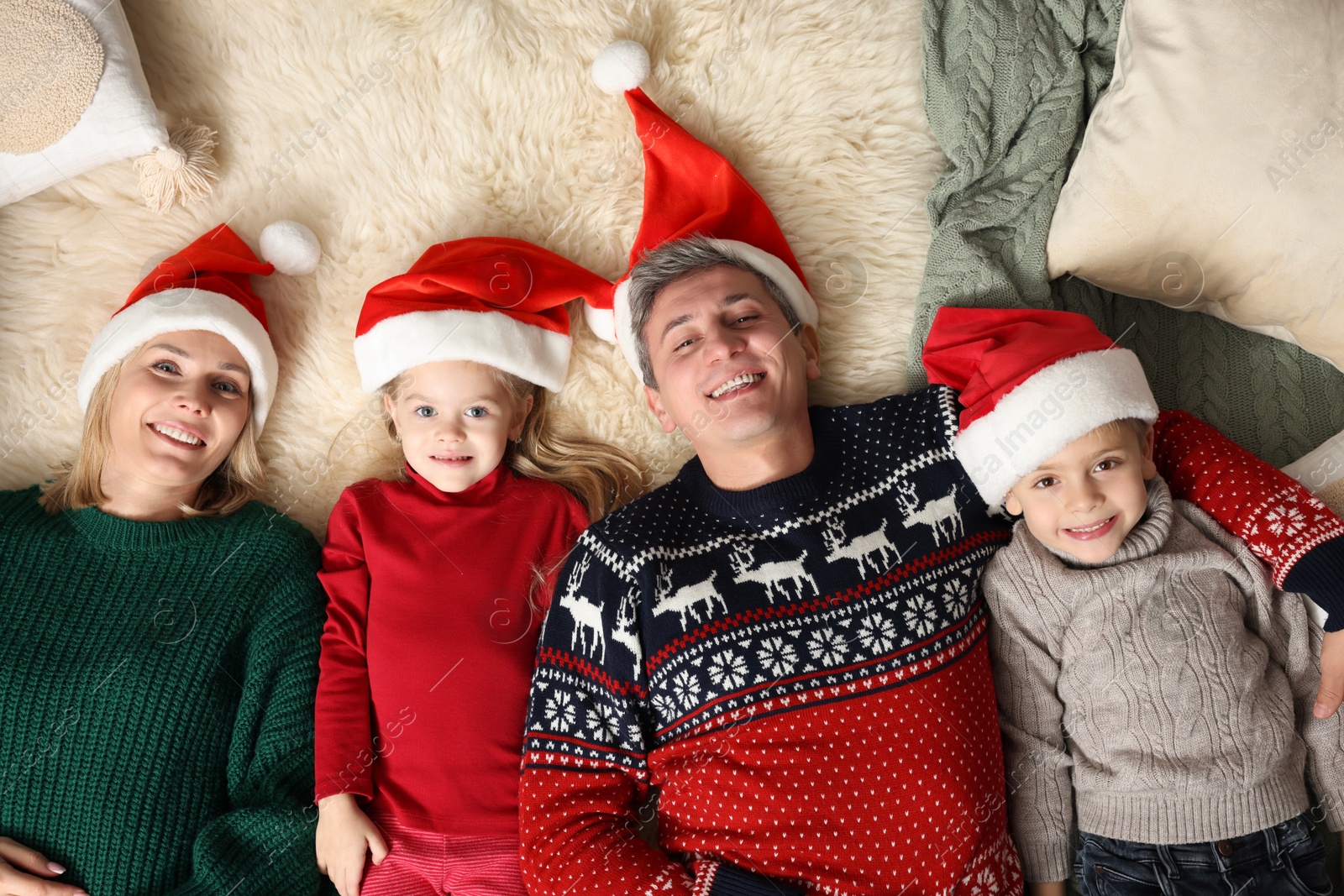 Photo of Happy family in Santa hats lying on rug together, top view. Christmas season