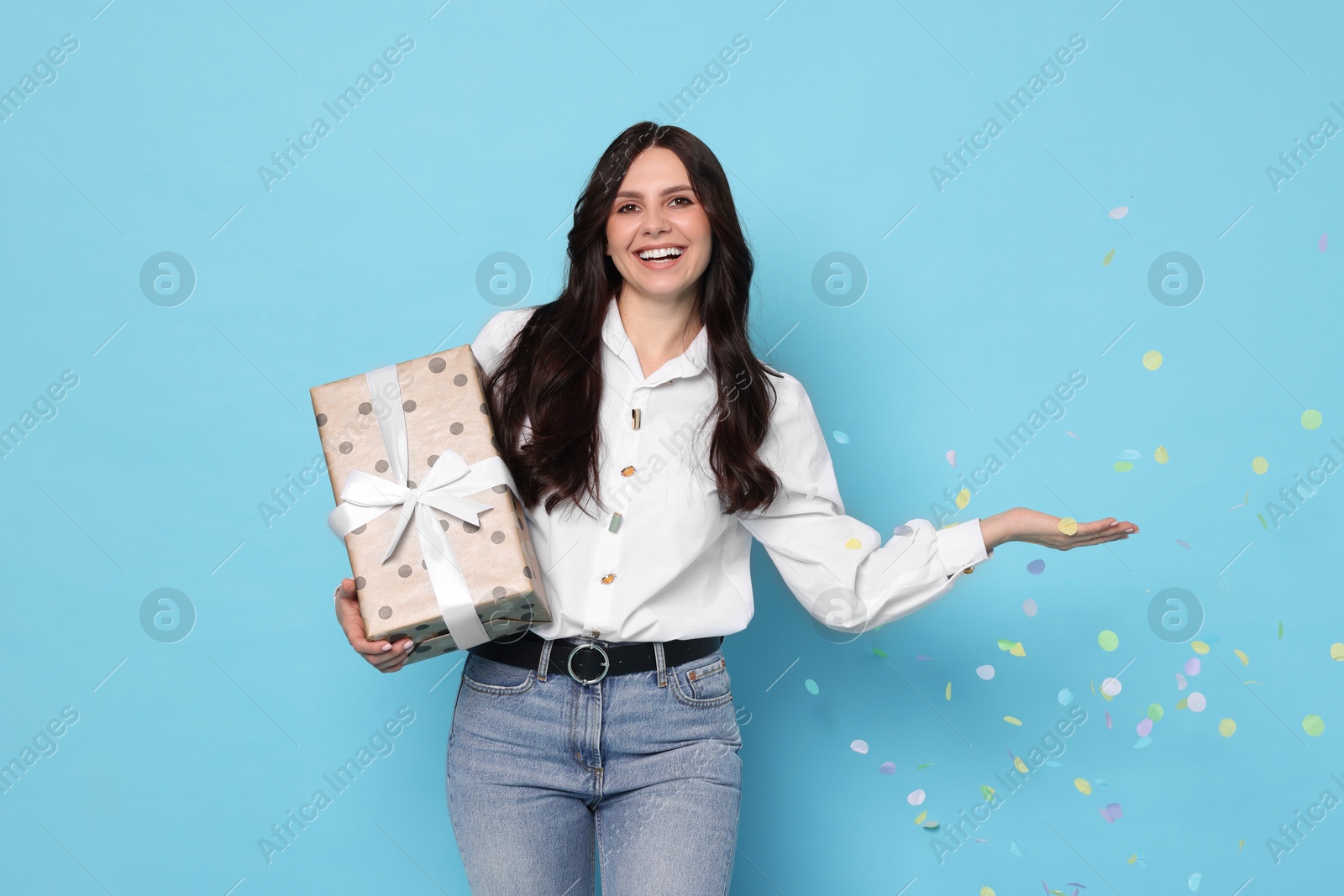 Photo of Happy woman with gift box and flying confetti on light blue background. Surprise party